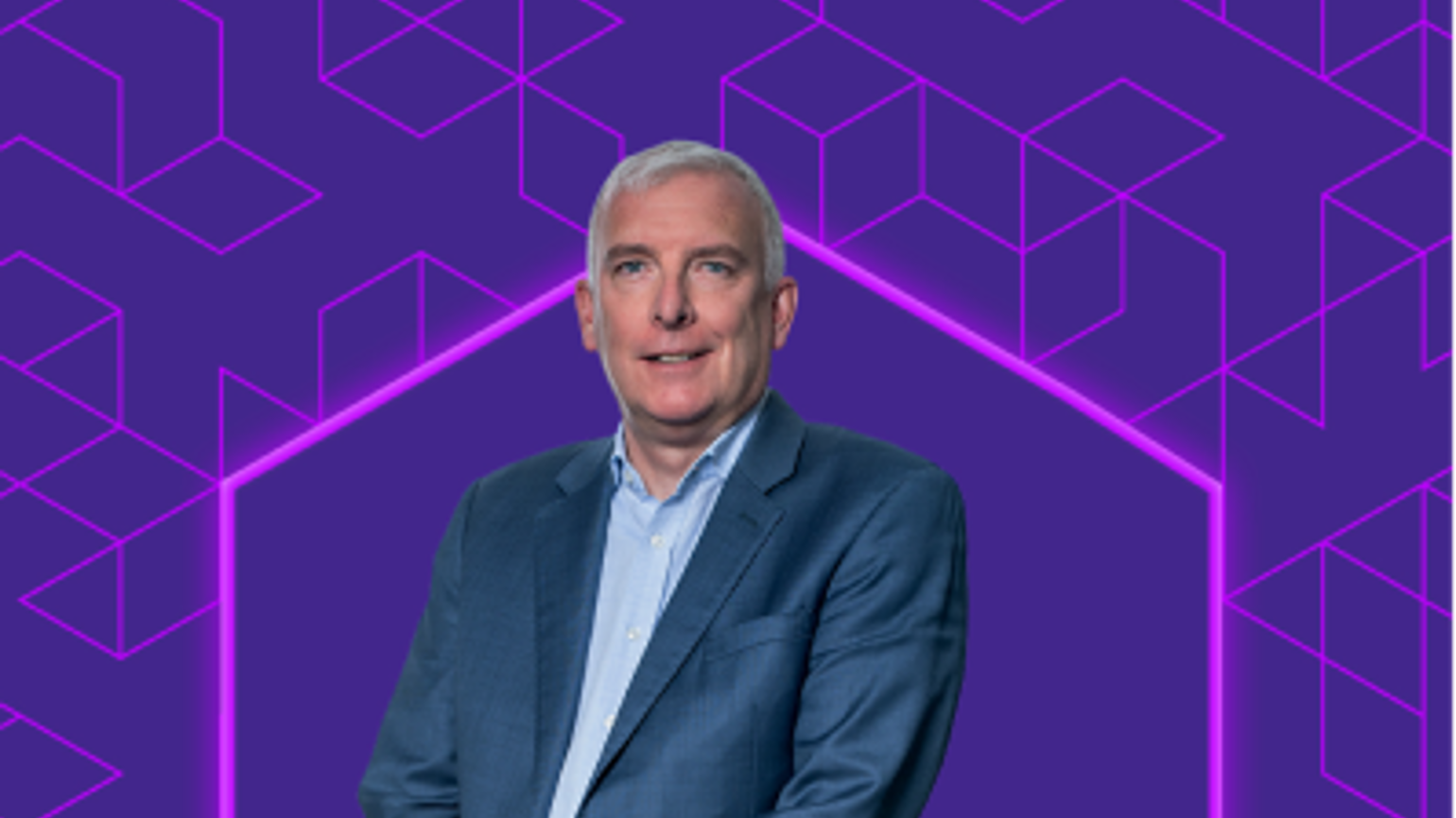 A man with white hair standing in with the background of Entain's design