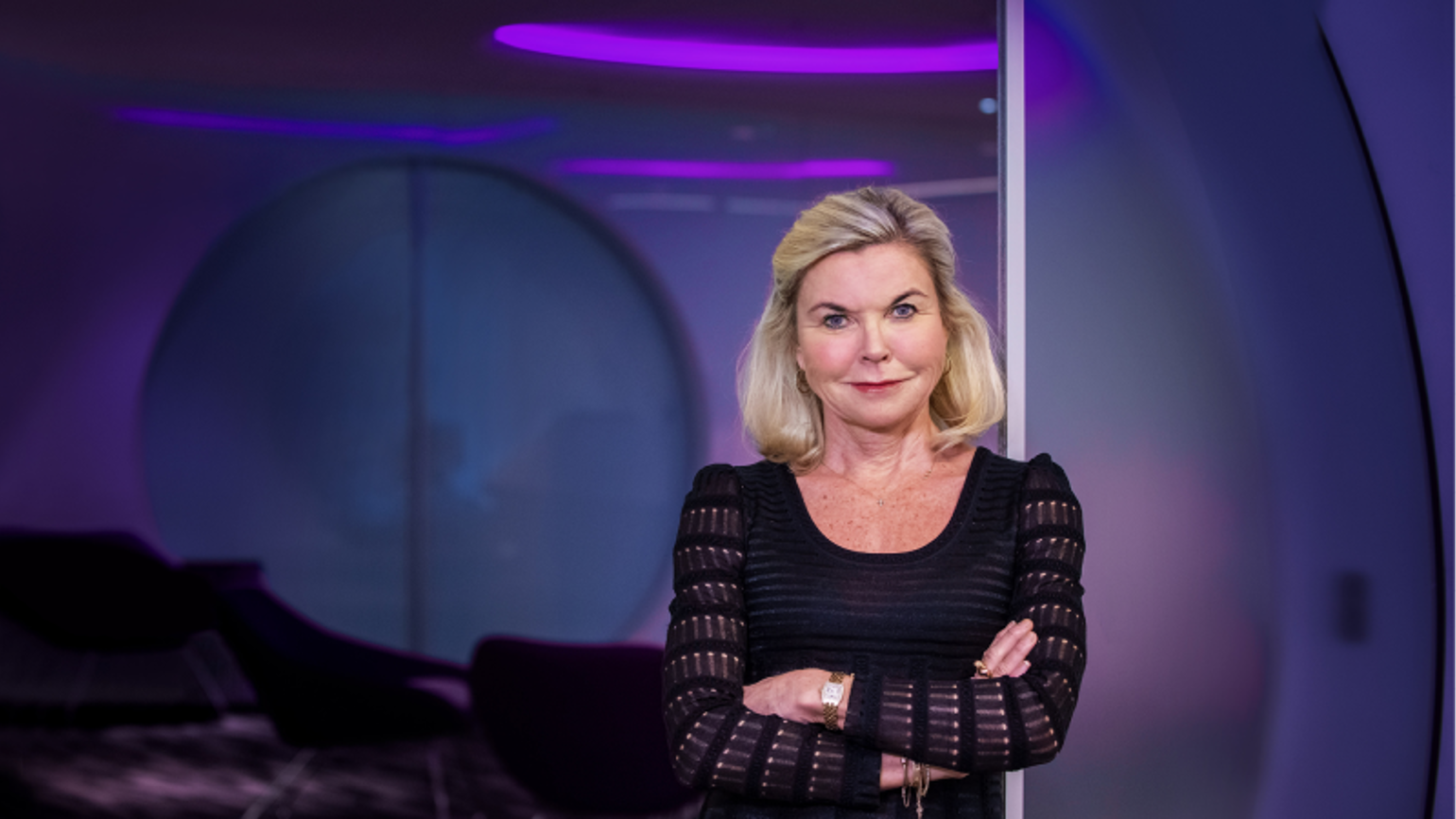 A blonde woman in a black dress folding her arms