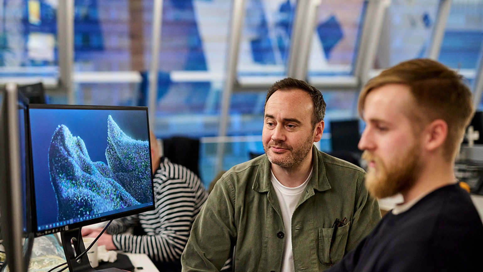 Two males sitting in an office environment looking at a computer screen together